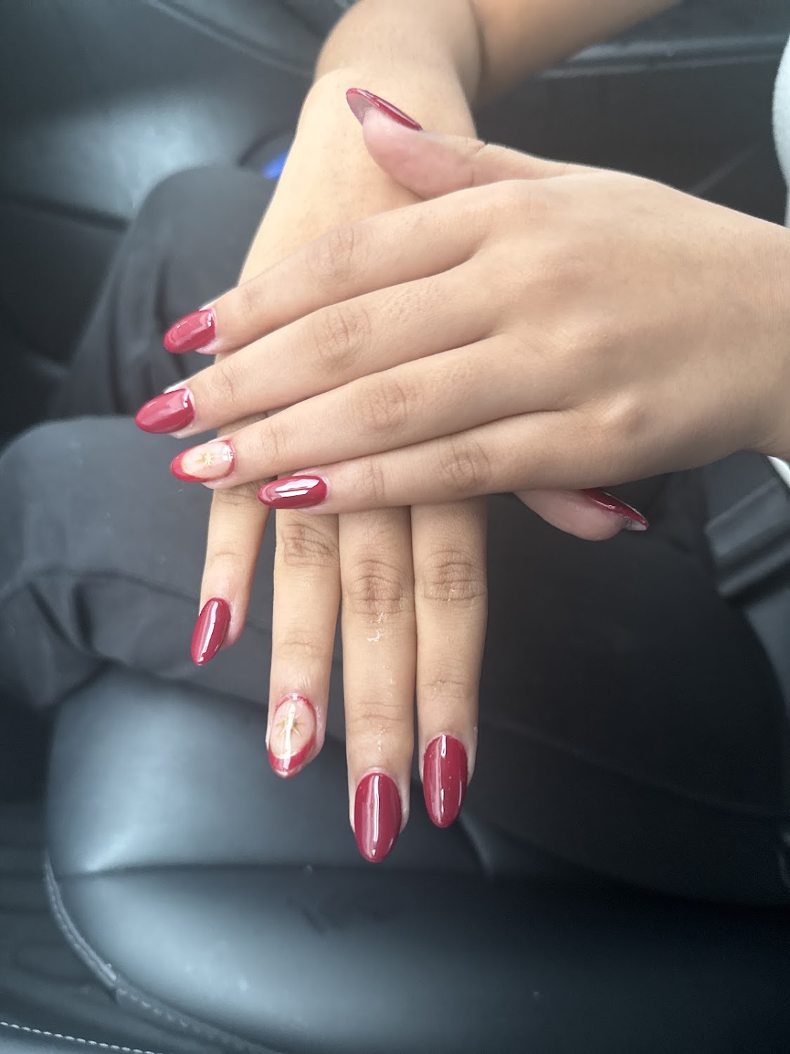 Two hands with glossy deep red almond nails, two of them finished with a small painted star accent.